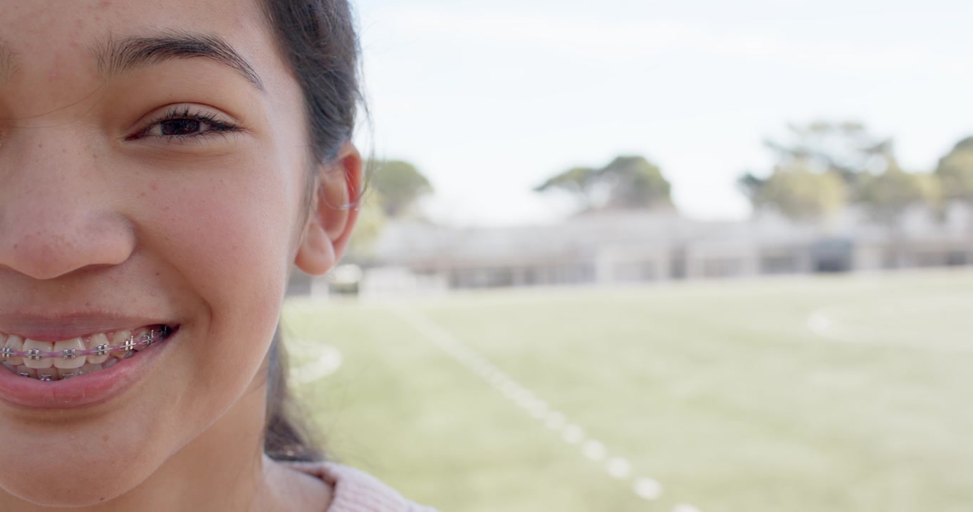 African American teen sun opening eye grinning revealing braces in pink top on field, copy space