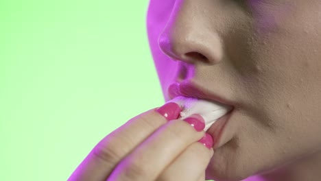 Close-Up-Of-Woman's-Mouth-Eating-Marshmallow-Against-Green-Background,-Studio-Shot