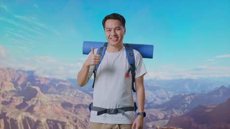 asian male hiker with mountaineering backpack smiling and showing thumbs up gesture to camera while traveling at the top of mountain