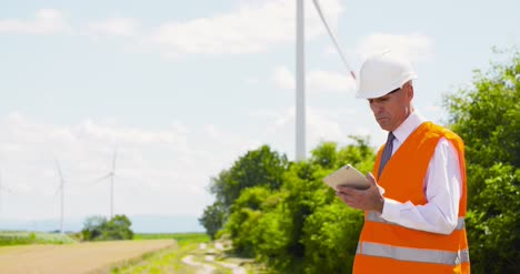 Ingeniero-Energético-Trabajando-En-Tableta-Digital-Contra-Molinos-De-Viento-Farm-8