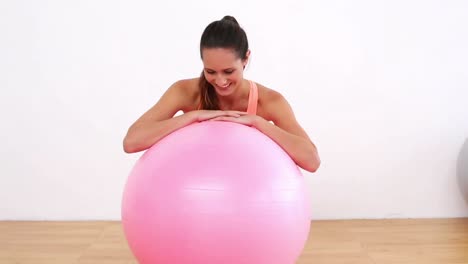 fit model leaning on pink exercise ball smiling at camera