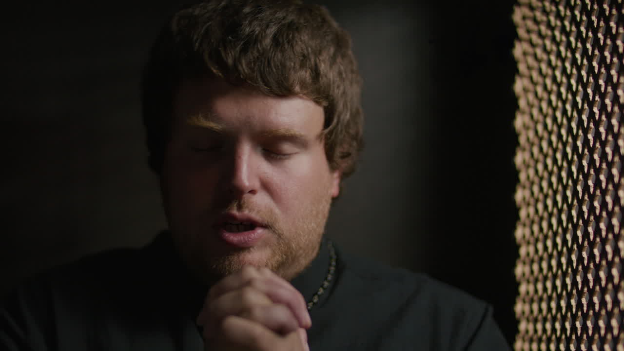Priest Praying with Hands Together inside Confessional Booth