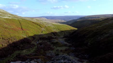 backwards-sweeping-drone-clip-from-the-bottom-of-a-lush-valley-behind-a-timelapesing-camera-,-then-showing-the-perfect-zig-zag-shadows-down-the-huge-lush-green-english-moorland-valley