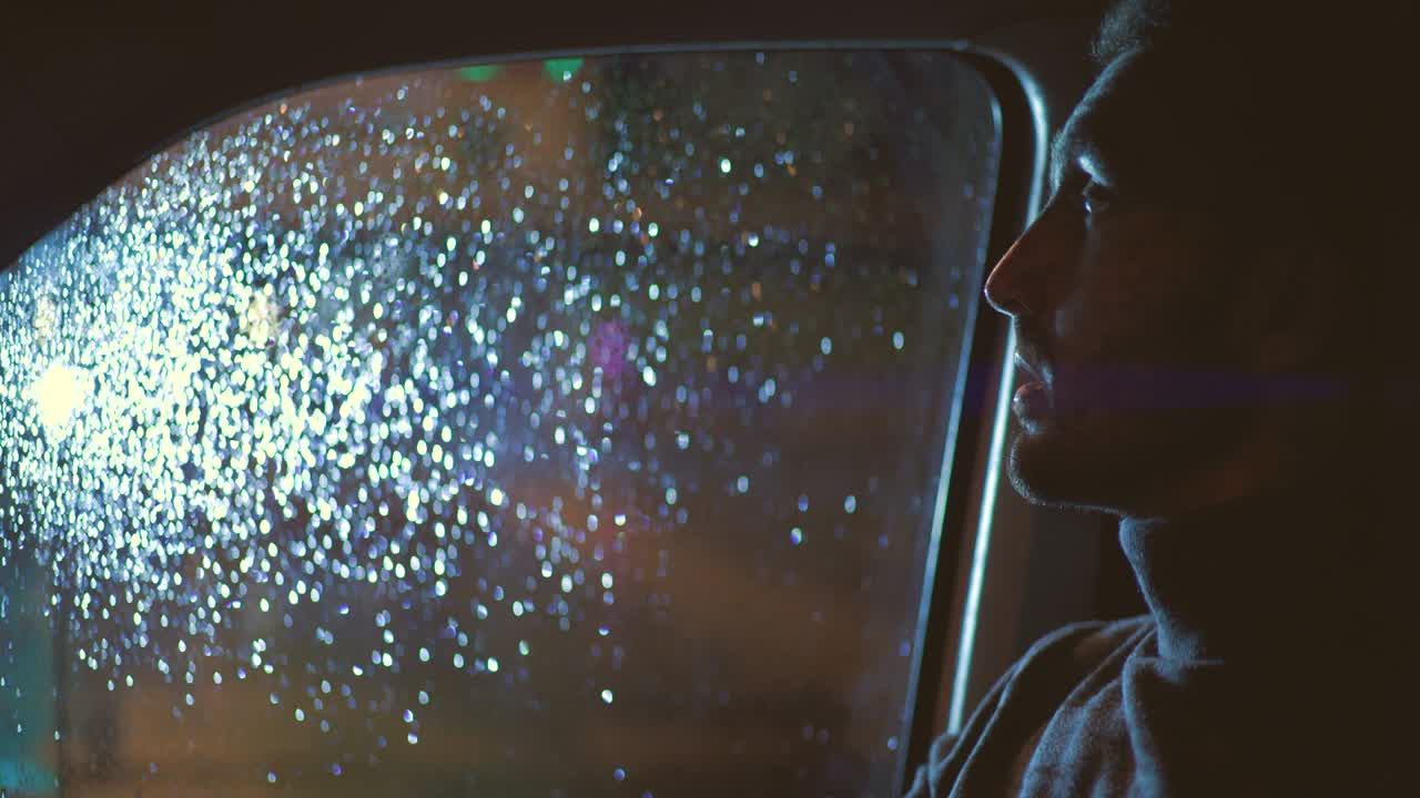 의료 마스크를 입은 남자는 비가 오는 밤에 차에 앉아 있습니다.