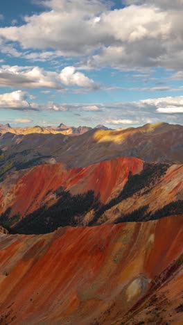 Vertikaler-4K-Zeitraffer,-Wolken-Und-Schatten-Bewegen-Sich-über-Einer-Atemberaubenden-Berglandschaft-Mit-Roten-Hügeln-Und-Grünen-Wäldern