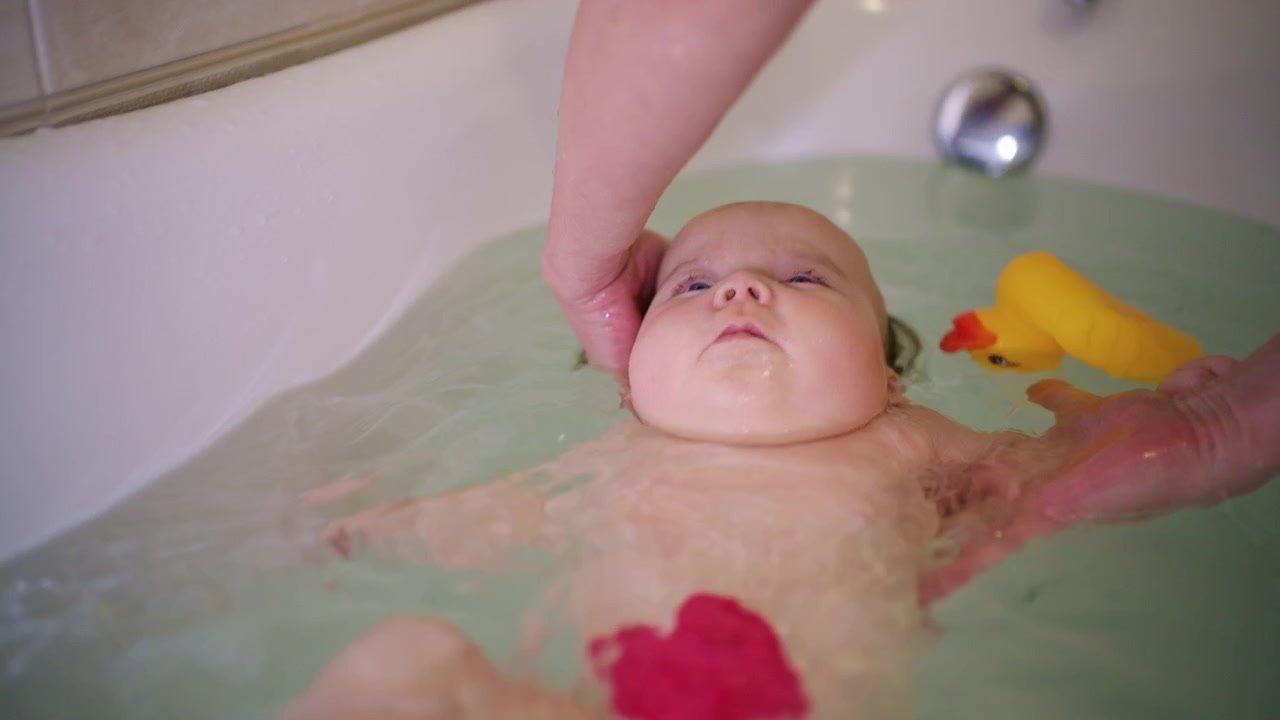 Close up of a baby enjoying bath time while being supported by an adult