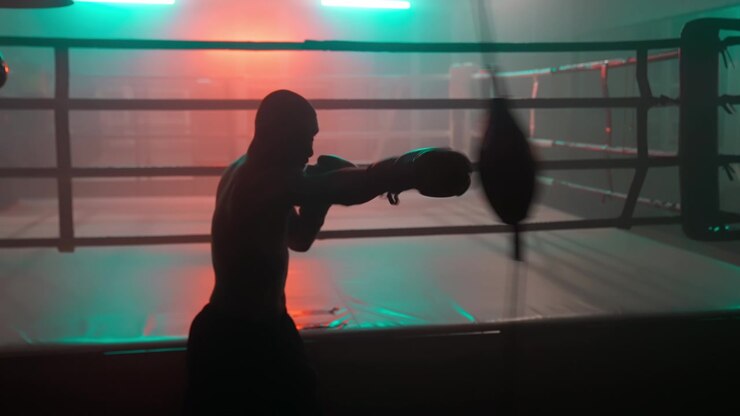 Silueta de boxeador entrenando con saco de velocidad en gimnasio oscuro con luces de neón