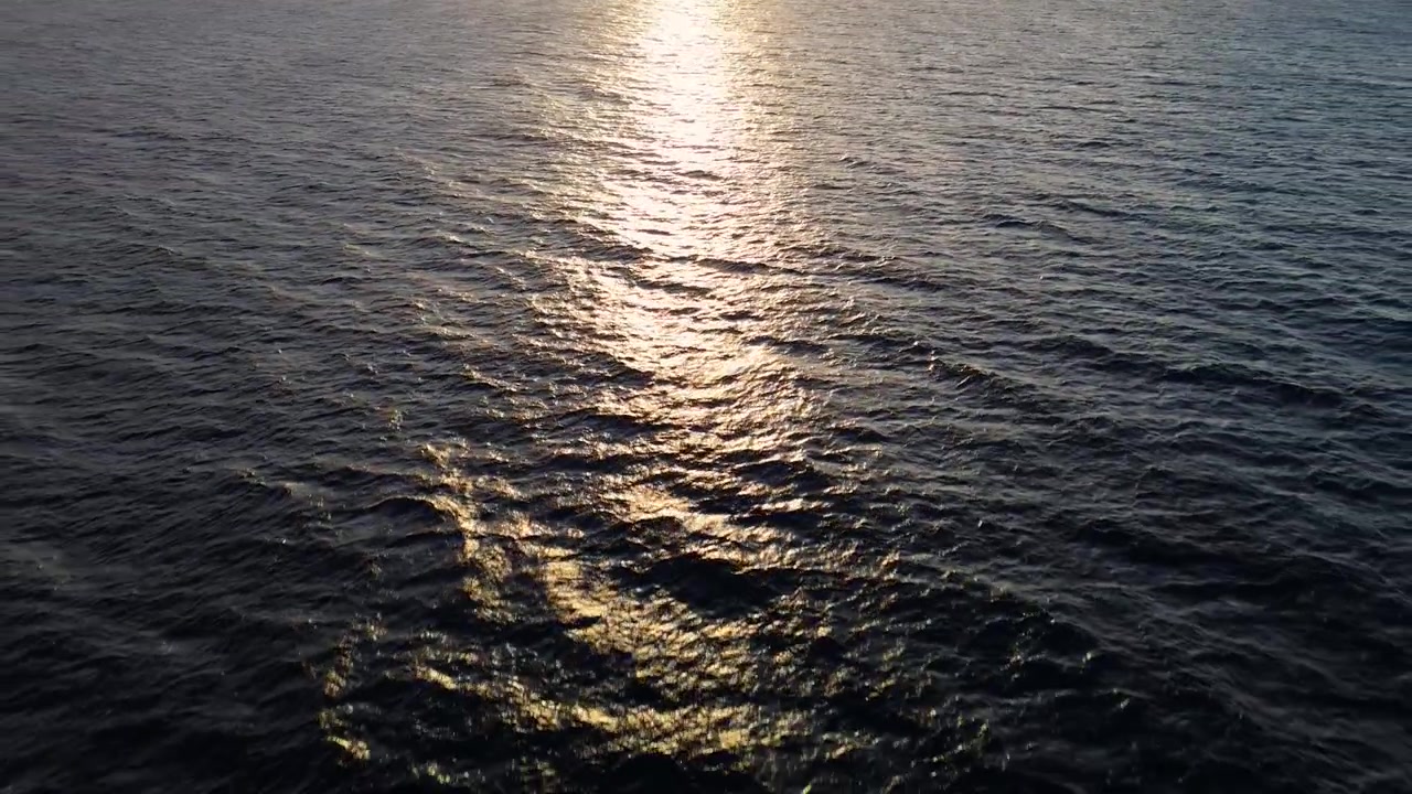 Drone aerial of sunset glow reflecting on the calm sea, peaceful waters at dusk