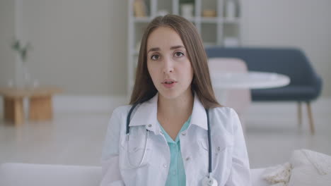 Una-Joven-Doctora-Sonriente-Usa-Un-Estetoscopio-Uniforme-Blanco-Consultando-A-Un-Paciente-En-Línea-A-Través-De-Una-Videollamada-Mirando-La-Cámara-Hablando-Por-Cámara-Haciendo-Video-Chat-A-Distancia-Telemedicina-Y-Concepto-De-Salud-Electrónica-Cámara-Web