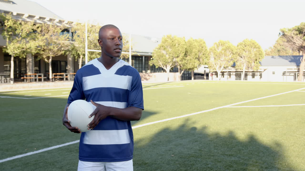 Holding soccer ball, african american male athlete standing on field in sports uniform, copy space