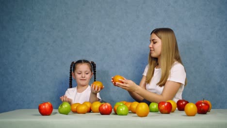 woman and little girl with healthy fruit. happy mother and daughter in white t-shirts playing with fresh organic fruits on blue background.
