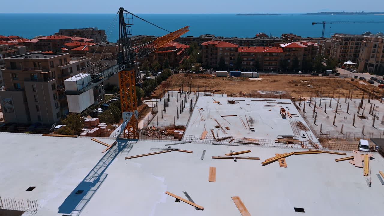 Coastal construction this summer. Construction workers are actively building a coastal structure with views of the sea and nearby urban landscape