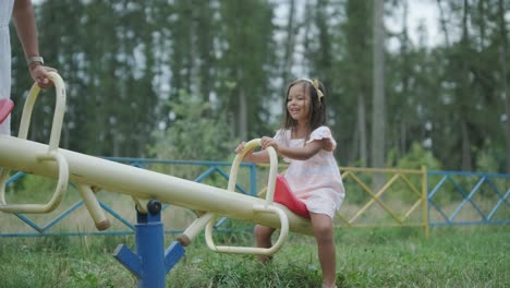 a pregnant mother and her young daughter enjoy playful time together at a playground in the park, surrounded by trees and greenery