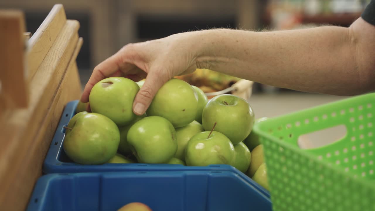 Store employee removing bruised and rotted apples from shelf at grocery store during daytime in Minnesota, USA.