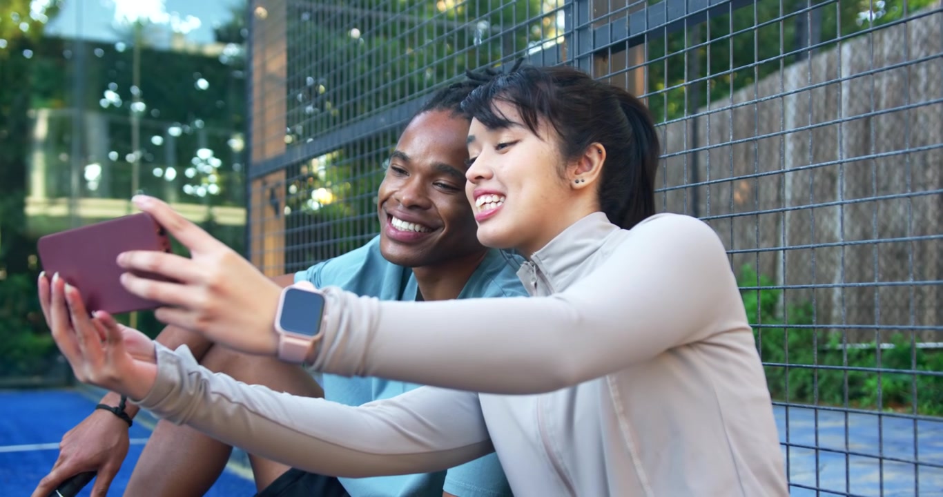 African American man, Asian woman on blue court, man gesturing, woman reaching phone to view screen