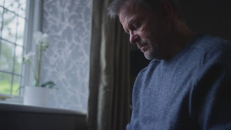 Unhappy-Mature-Man-Trying-To-Keep-Warm-By-Radiator-At-Home-During-Cost-Of-Living-Energy-Crisis