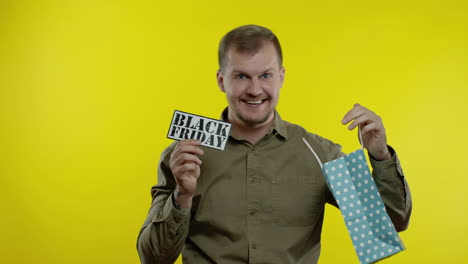 man showing black friday inscription from shopping bag, smiling, rejoicing discount, low prices