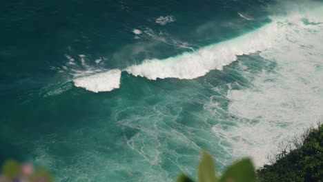 large wave breaks at tropical shore of bali, seen from top of cliff, blue water