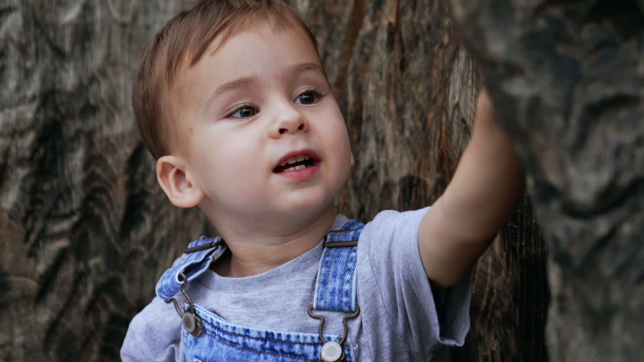 Adorable Caucasian kid sits outdoors with a book. Lovely toddler hides his face behind the book. Close up.