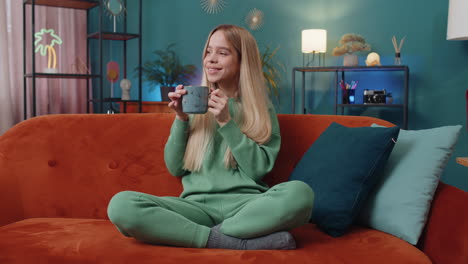 Attractive-smiling-woman-girl-drinking-a-cup-of-coffee-or-herbal-tea-at-home-couch-in-the-morning