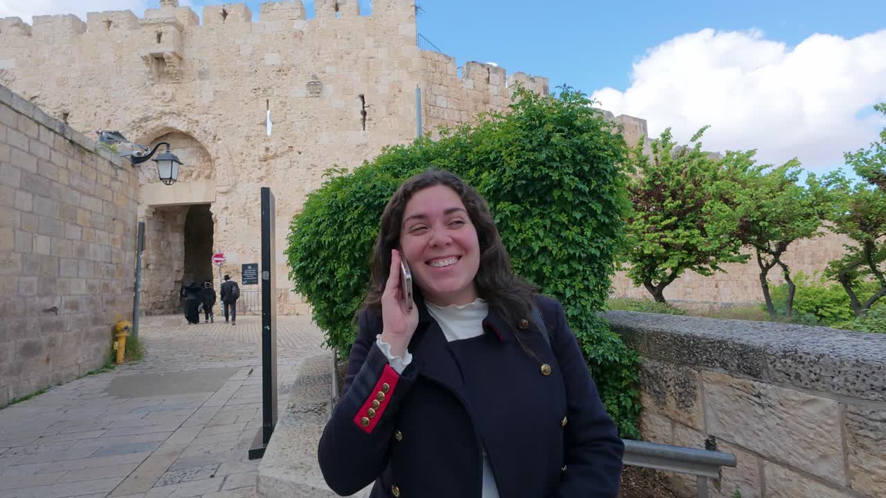 Young adult woman talking on phone near Jerusalem old city walls, Zion Gate. Slow motion.