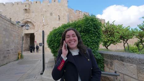 young adult woman talking on phone near jerusalem old city walls, zion gate. slow motion.