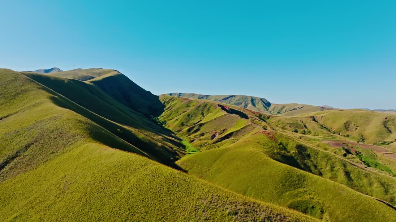 Aerial footage showcasing the rolling green hills and dramatic terrain of Madagascar under a clear blue sky, perfect for nature lovers and travel enthusiasts.
