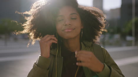 portrait of beautiful trendy african american woman puts on earphones listening to music enjoying sunset in windy urban city