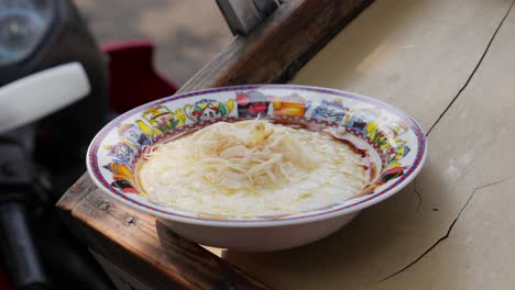 une pince plaçant du poulet haché sur du porridge de riz dans un bol coloré sur une surface en bois