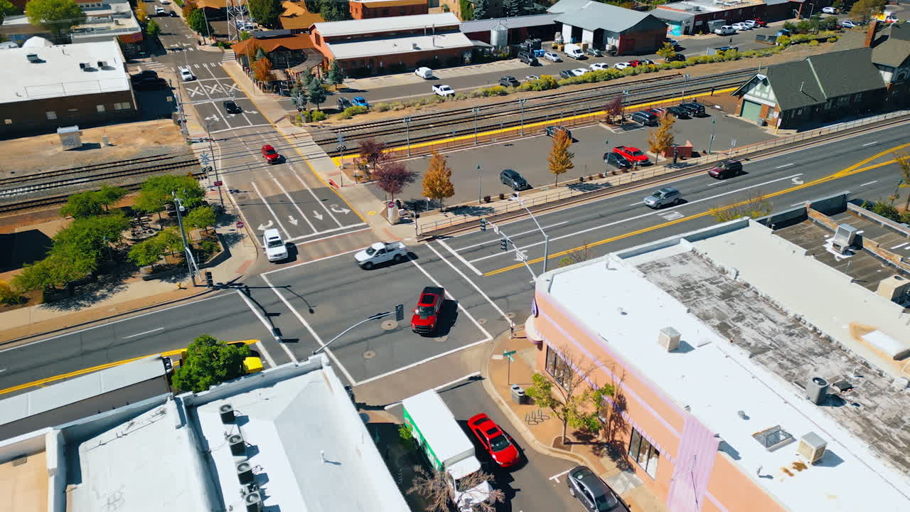 Cars ride by the roads and crossroad of a cozy city. Railways are along the highway. Flagstaff, Arizona, USA. Aerial view