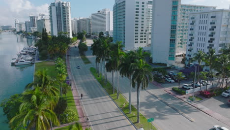 Modern-luxurious-neighbourhood-in-tropical-area.-Cars-driving-on-multilane-road-leading-between-high-rise-apartment-buildings.-Miami,-USA