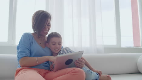 Mutter-Und-Sohn-Sitzen-Auf-Dem-Sofa-Und-Benutzen-Ein-Digitales-Tablet.-Glückliche-Mutter-Und-Kleiner-Junge-Benutzen-Ein-Tablet-Mit-Touchscreen-Und-Schauen-Gemeinsam-Ein-Video-An.-Lächelnde-Mutter-Und-Süßer-Junge-Spielen-Mit-Einem-Digitalen-Tablet.