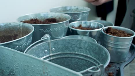 a man with a tattooed arm is scattering soil across the buckets, distributing it evenly with deliberate movements