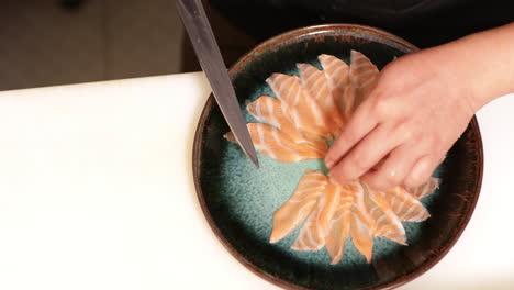 arranging slices of fresh raw salmon for sashimi serving in a plate in a sushi restaurant - high angle shot, slow motion