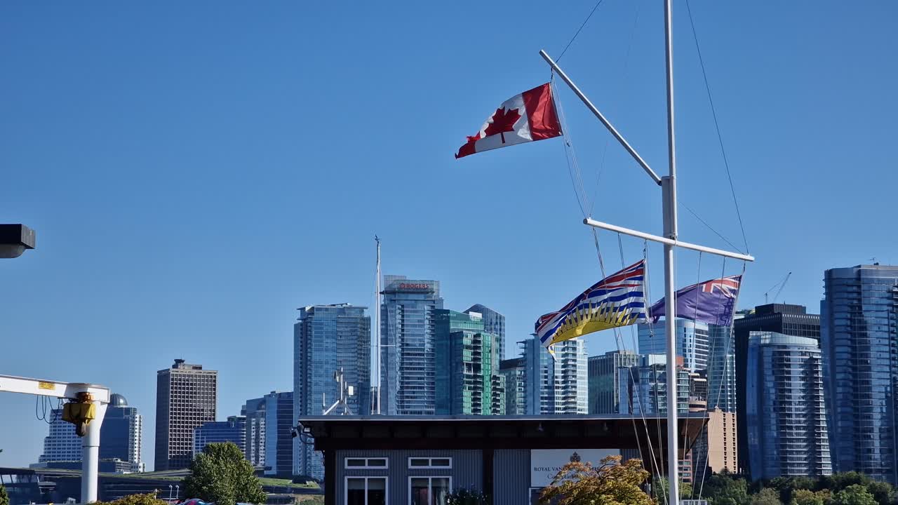 Canadisk flag vajer i Stanley Park om dagen med højhusbygninger i baggrunden - Vancouver, British Columbia, Canada.