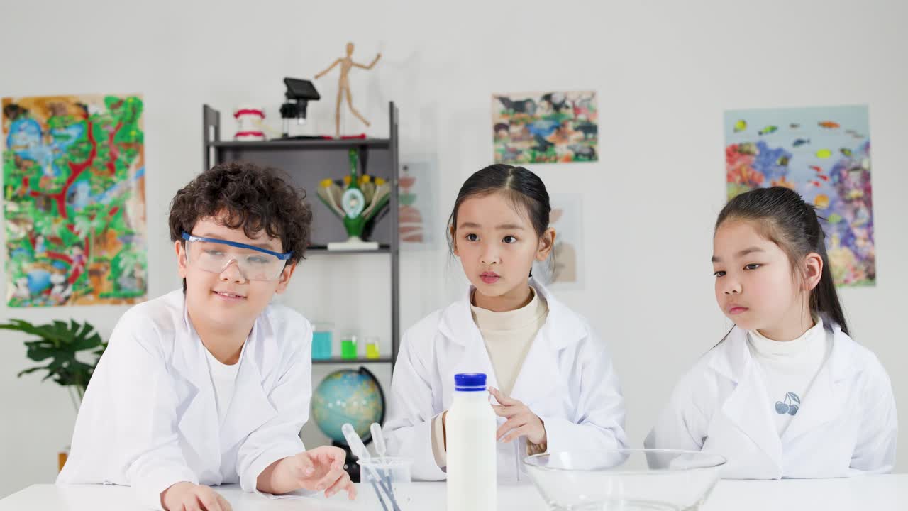白衣と安全ゴーグルを着用した3人の若い学生が、科学実験について一緒に話し合っている