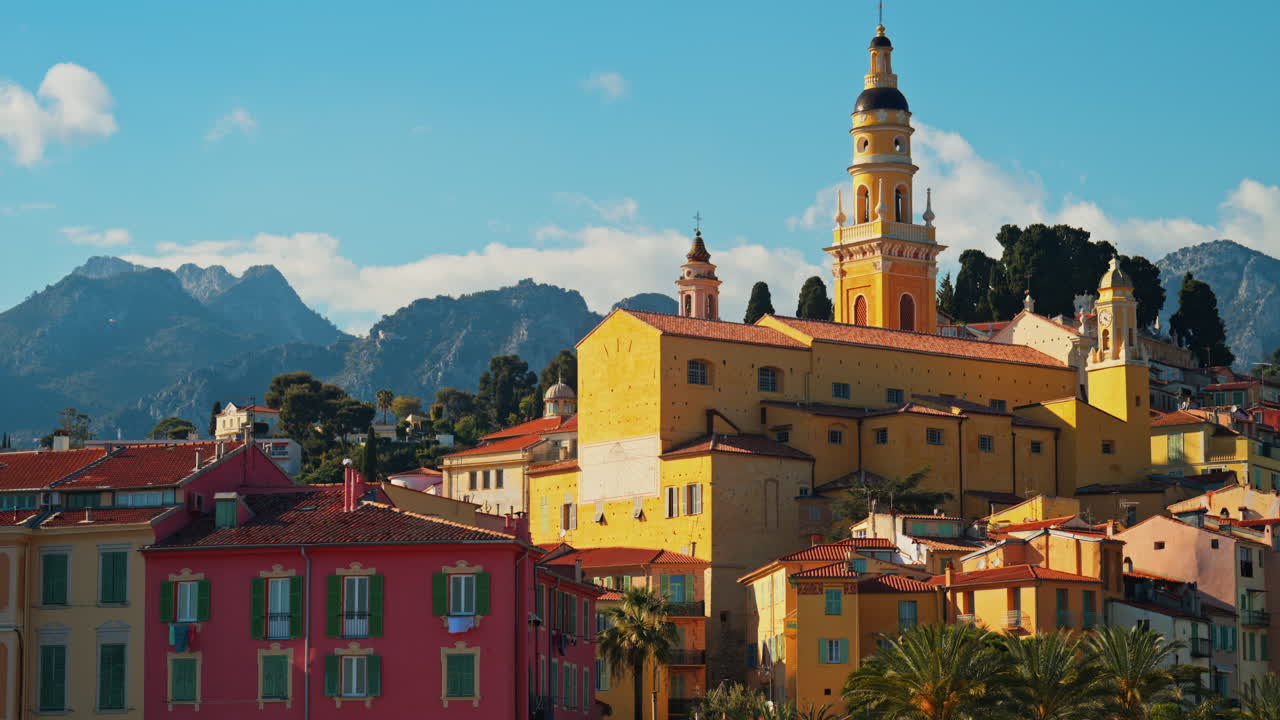 Distant view of the St Michel Basilica surrounded by colourful buildings and palm trees, Menton, France