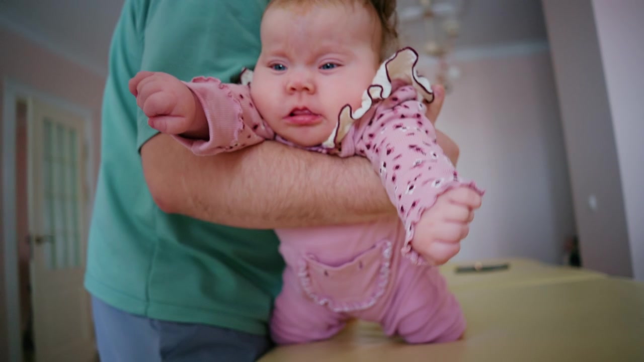 Close-up de um bebê sendo gentilmente segurado na vertical em uma maca de tratamento acolchoada durante uma sessão de terapia pediátrica.