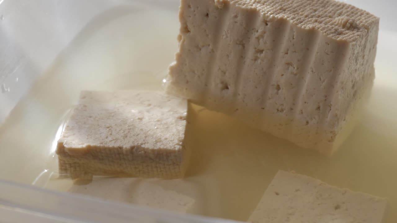 Tofu cubes soaking in water inside a container, with a close-up view of the texture