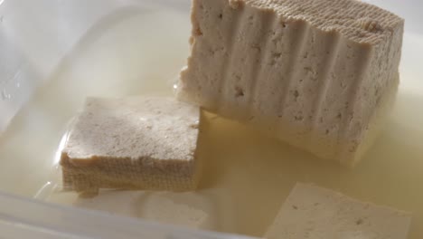 tofu cubes soaking in water inside a container, with a close-up view of the texture