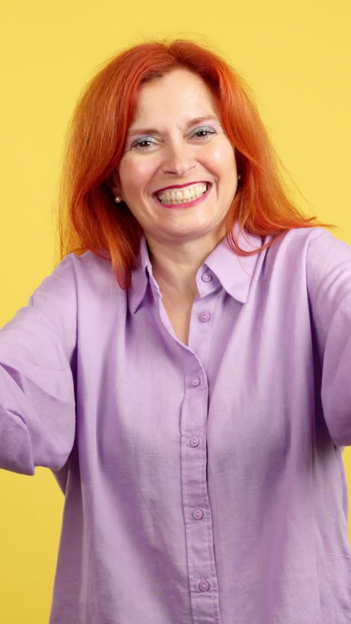 A red-haired woman blowing a kiss and laughing against a yellow background