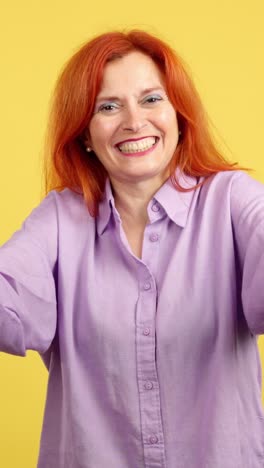a red-haired woman blowing a kiss and laughing against a yellow background