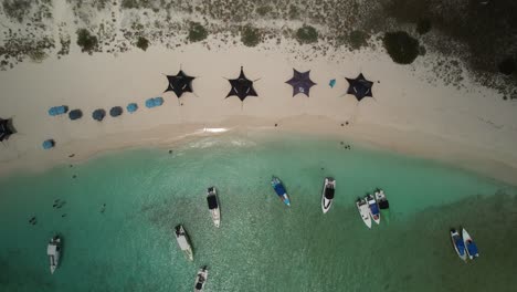 Ein-Tropischer-Strand-Mit-Booten-Und-Sonnenschirmen-Auf-Weißem-Sand-Und-Türkisfarbenem-Wasser,-Luftaufnahme