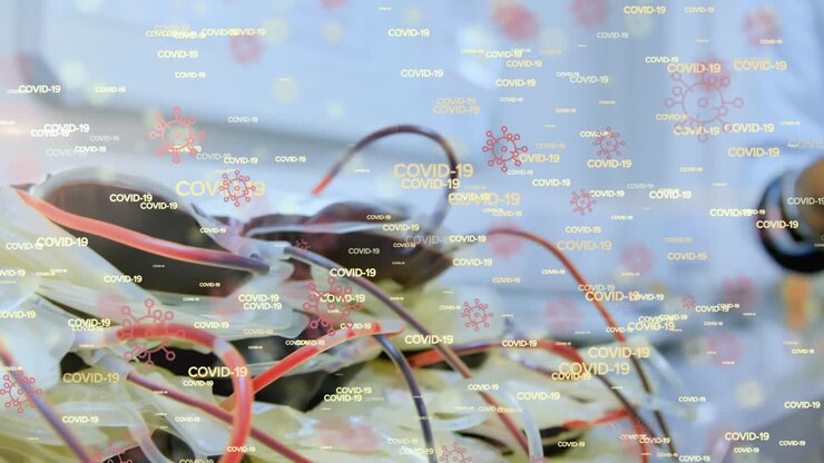 Animation of floating Covid-19 cell icons and words over biracial doctor holding a blood bag