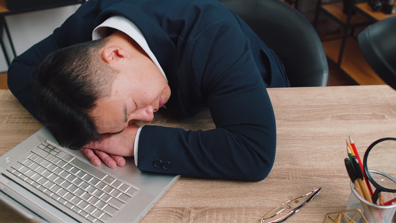 Bored sleepy business man worker working on laptop leaning on hands falling asleep at office table