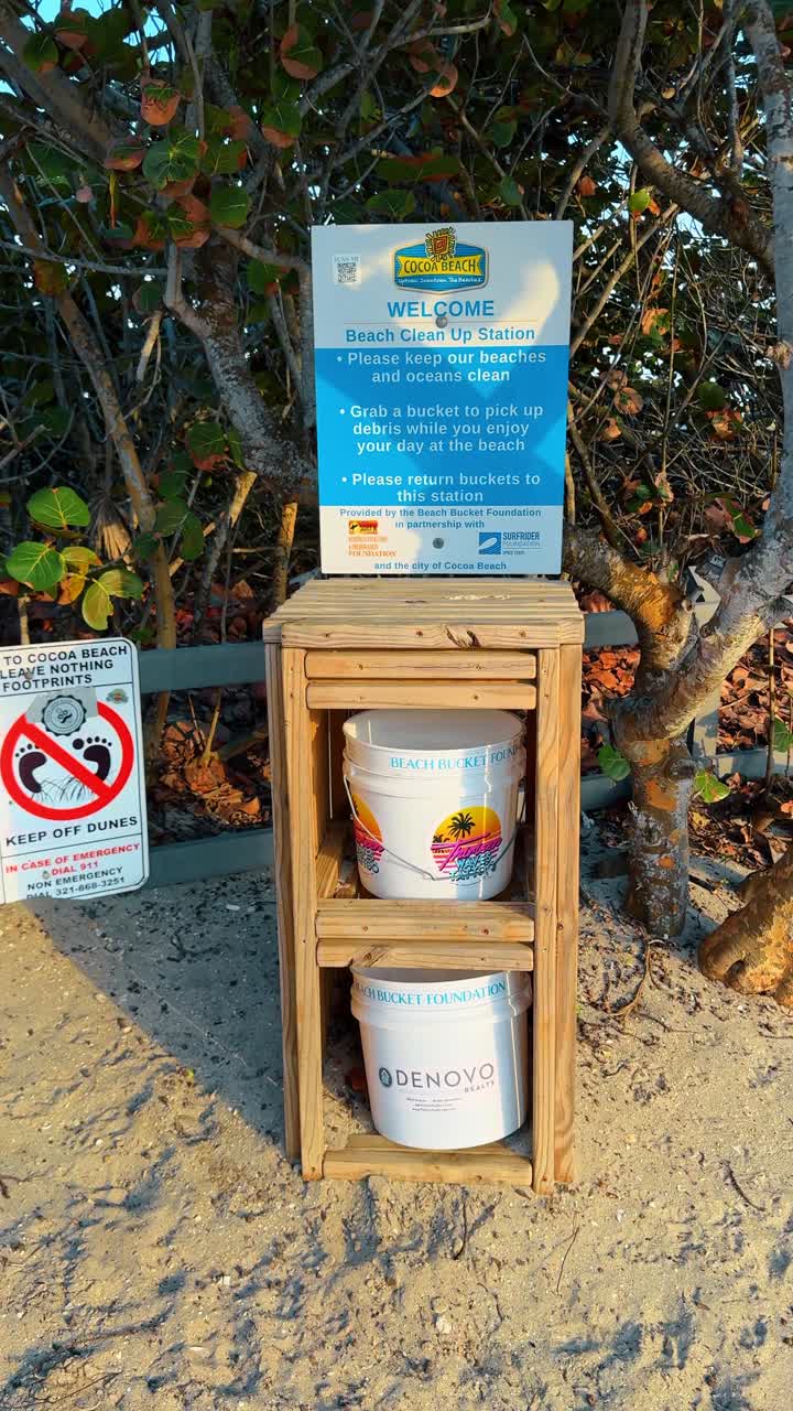 Orlando, EE. UU., 9 de junio de 2025: Estación de limpieza de playa con cubos en Cocoa Beach, Florida. Soporte de madera que sostiene cubos de plástico para recoger escombros en la entrada de una playa de arena.