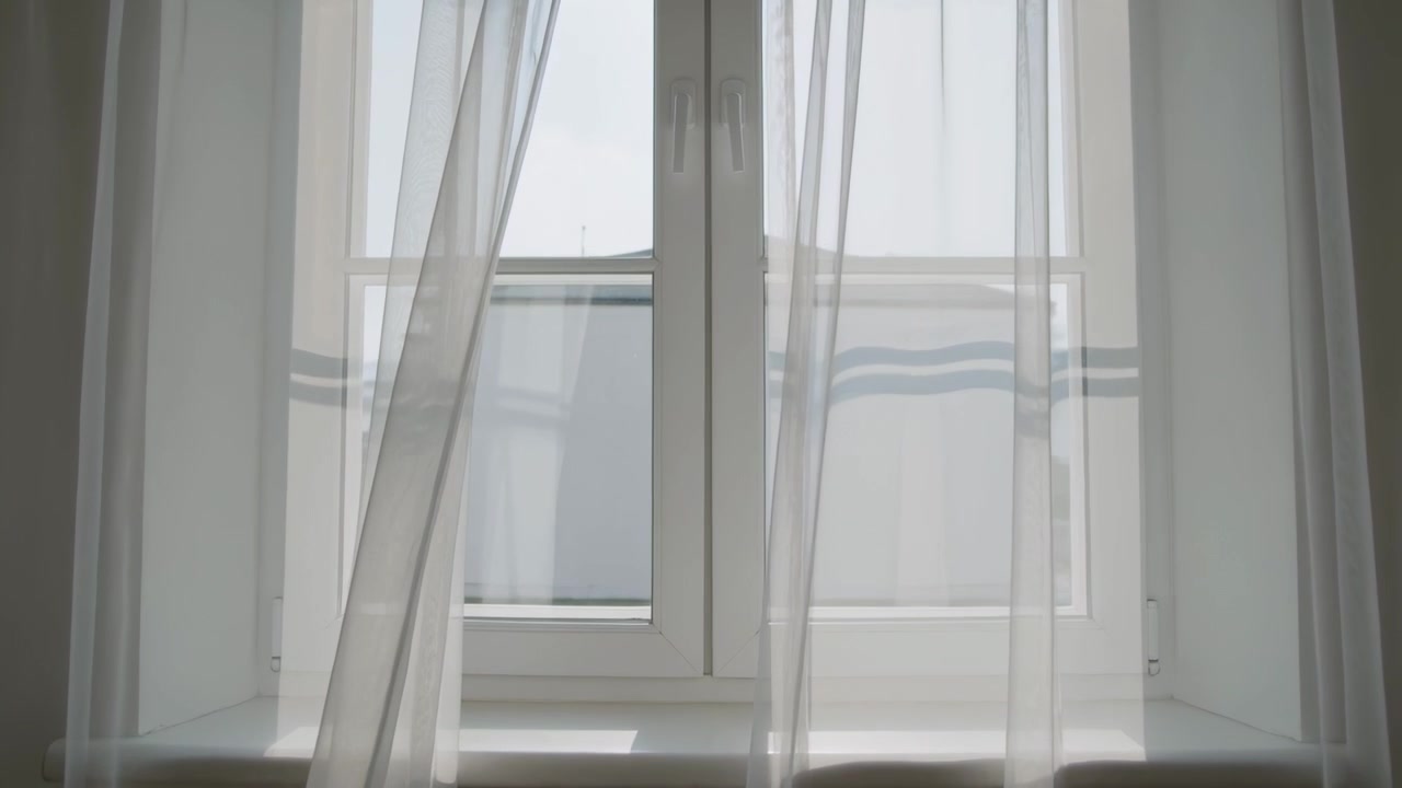 Breeze entering recessed window alcove nudging sheer curtains inward, showing panel and roofline