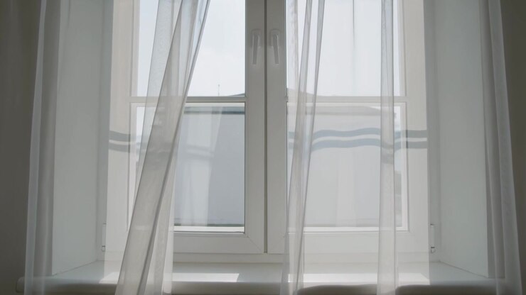 Breeze entering recessed window alcove nudging sheer curtains inward, showing panel and roofline