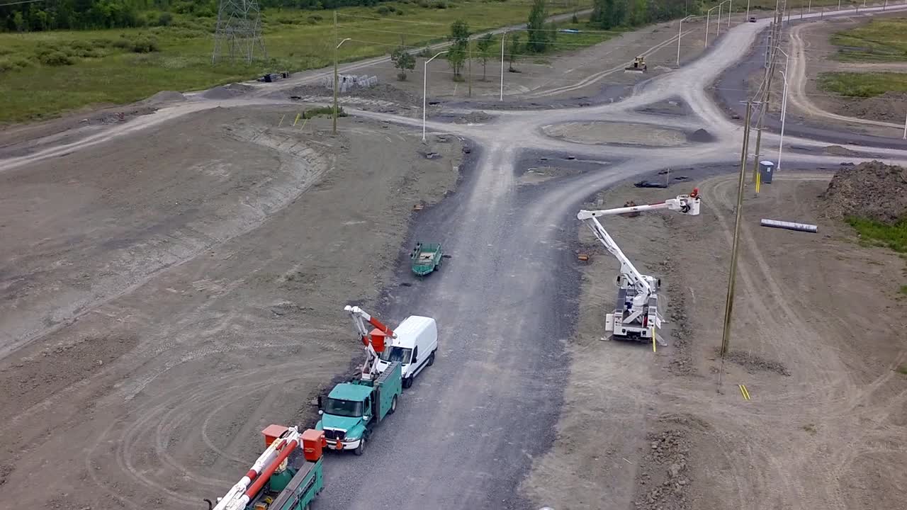 workers install telephone poles in bucket truck along a newly constructed road with a roundabout