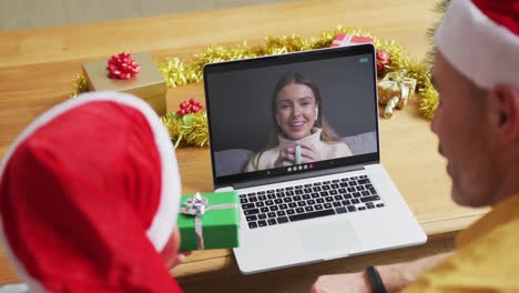 Caucasian-father-and-son-with-santa-hats-using-laptop-for-christmas-video-call-with-woman-on-screen